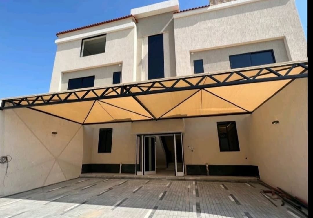 مظلة فناء واسعة بهيكل جمالوني وقماش مشدود على مدخل منزل